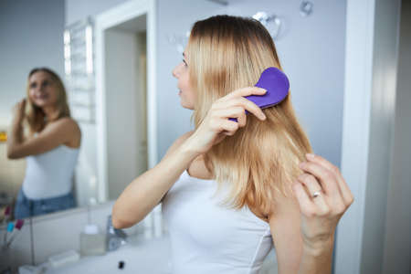 Blonde young woman brushing hair at home