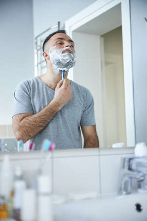 Good-looking man shaving beard in bathroom at homeの写真素材