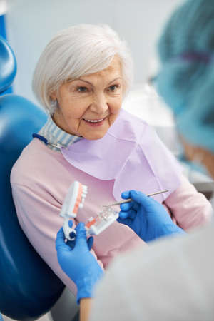 Interested pensioner looking at dentist with dental modelの写真素材