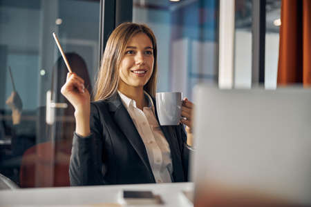 Pleased employee with a coffee mug sitting at the desk