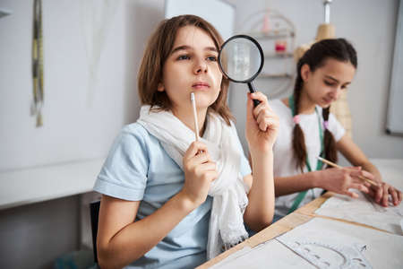 Adorable girl with magnifying glass working in sewing workshop