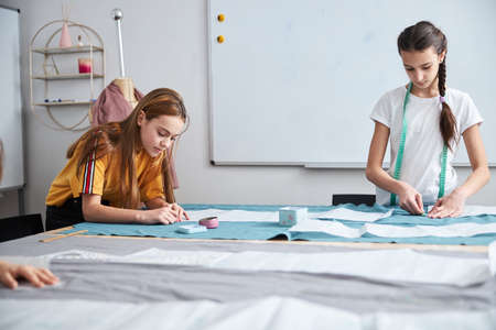 Adorable girls preparing fabric in sewing workshop
