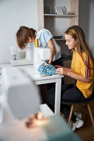 Adorable female children sewing clothes in workshopの写真素材