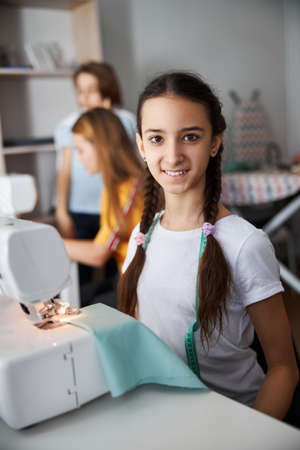 Cute joyful girl sewing clothes in workshopの写真素材