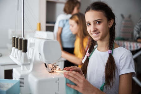 Cheerful female child sewing clothes in workshopの写真素材