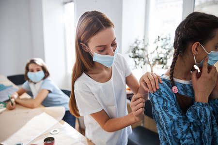 Female children in medical masks fitting dress in sewing studio