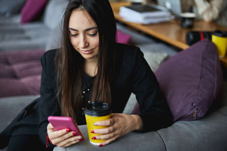 Beautiful young woman drinking coffee and using cellphone