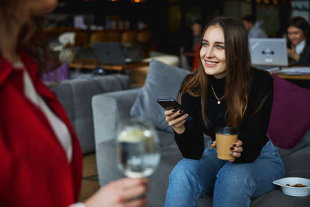 Charming young woman using cellphone and talking with colleague