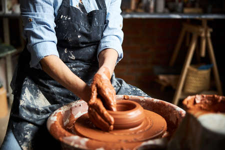 Old woman in apron making pottery in workshop