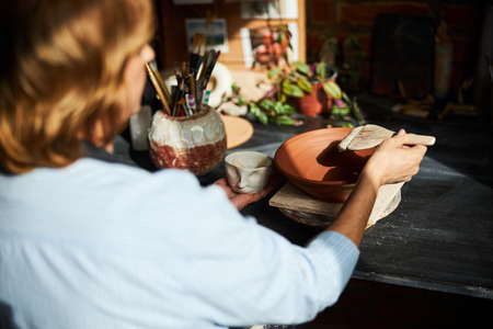 Senior woman ceramist painting pottery in workshop