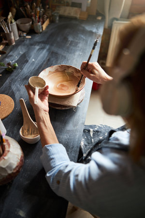 Senior woman ceramist painting pottery in workshop