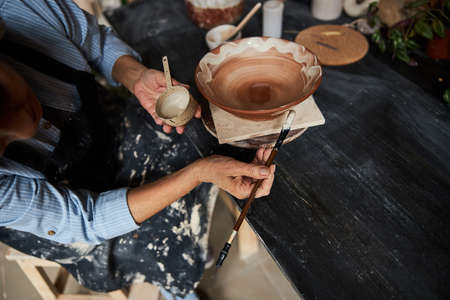 Female ceramic artist painting clay bowl in pottery studio