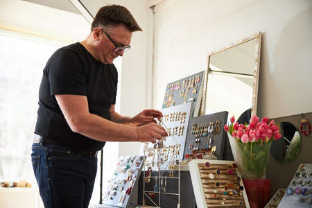 Male jeweler arranging his new jewels on the display stand