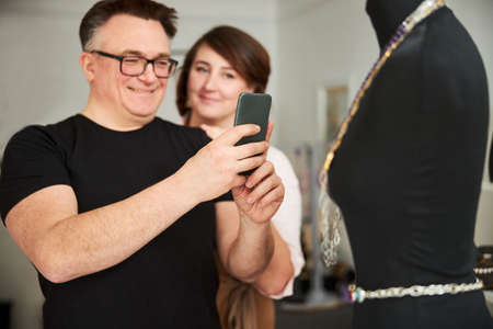Joyous man photographing his jewelry items on the cellphone