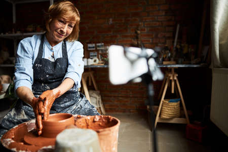 Nice senior woman making clay pot on pottery wheel