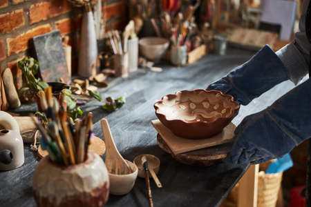 Potter hands placing painted bowl on table in pottery workshop