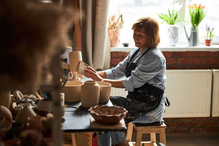 Charming old woman polishing pottery in workshop