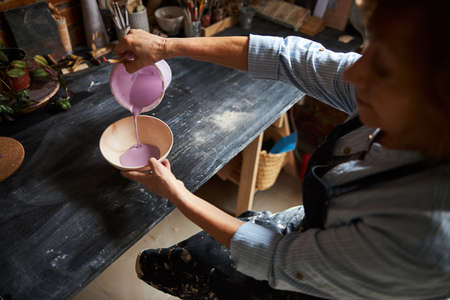 Female potter painting clay bowl in pottery workshop