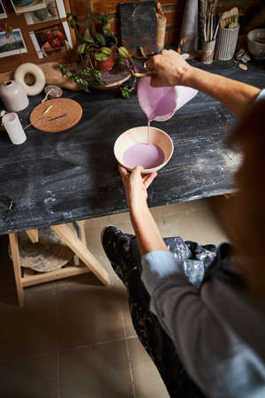 Female potter pouring pink paint on clay bowl in workshop