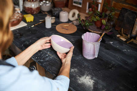 Female ceramic artist painting clay bowl in workshop