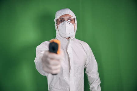 Young man in protective mask and suit holding digital thermometer