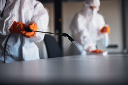 Janitorial workforce in hazmat suits sanitizing the office desksの写真素材