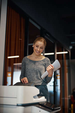 Lovely pleased young Caucasian secretary printing documents