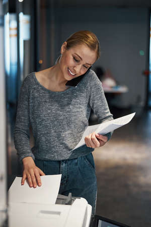 Smiling secretary printing documents during the phone conversation