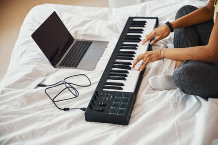 Young woman playing synthesizer and using laptop at homeの写真素材