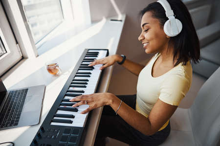 Beautiful Afro American woman playing synthesizer at homeの写真素材