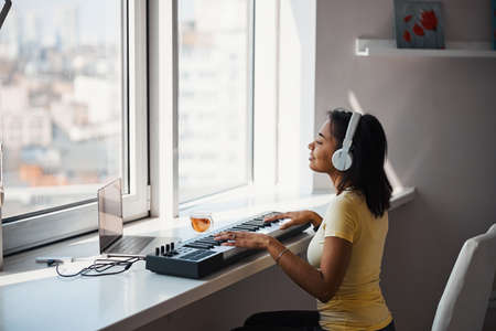 Beautiful young woman playing synthesizer at homeの写真素材