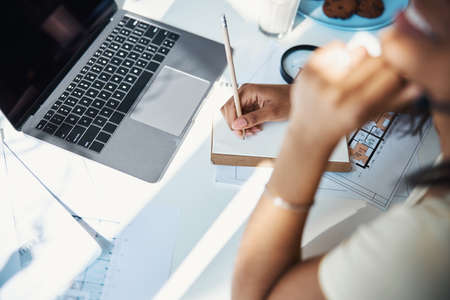 Afro American young woman using laptop and writing in notebook