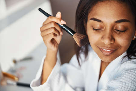 Cheerful young woman doing makeup at home