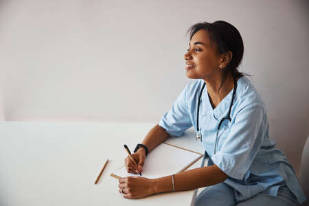 Cheerful female doctor writing on clipboard in clinic