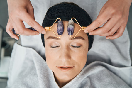 Tranquil spa client being massaged with amethyst face rollersの写真素材