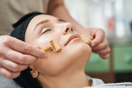 Cosmetician massaging the client face with acupressure metal roller massagersの写真素材