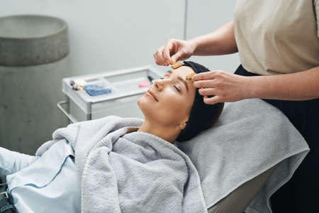 Cosmetician massaging her client forehead with acupressure metal roller massagersの写真素材