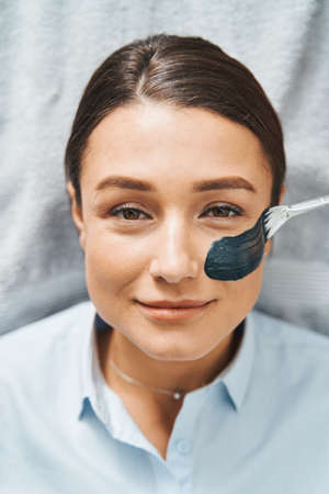 Cosmetician applying a charcoal mask on the patient cheekの写真素材