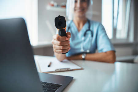 Cheerful female doctor using digital thermometer in clinicの写真素材