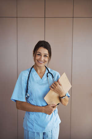 Cheerful female doctor with clipboard standing in clinicの写真素材