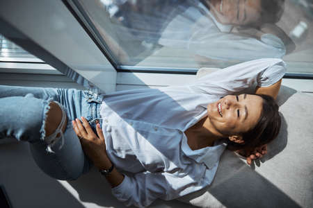 Beautiful cheerful woman resting on windowsill at home