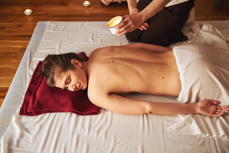 Massagist bringing massage candle to naked female backの写真素材