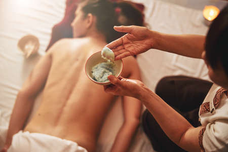 Masseuse picking up massaging mix from a bowl with fingersの写真素材