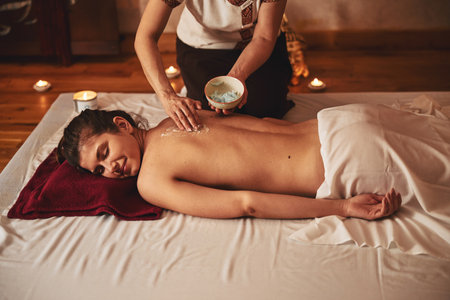 Adult spreading cream for massage on back of femaleの写真素材