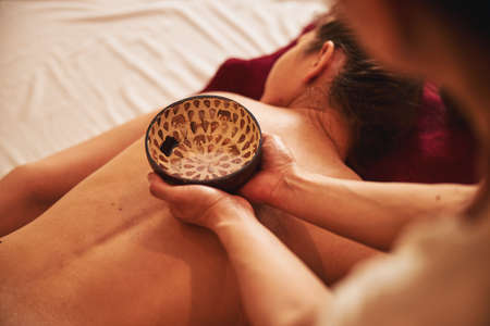 Liquid for massage inside of bowl lying on female backの写真素材