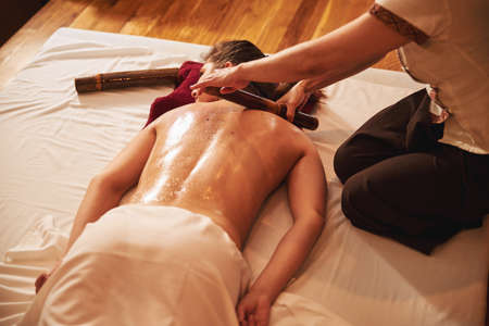 Treatment of woman back with wooden massage rollerの写真素材