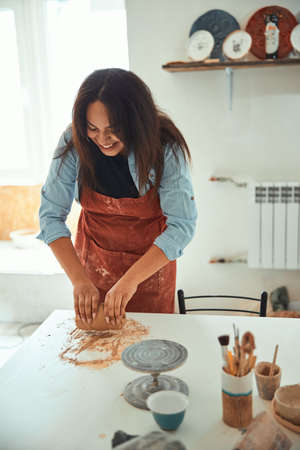 Cheerful woman in apron working in pottery workshop