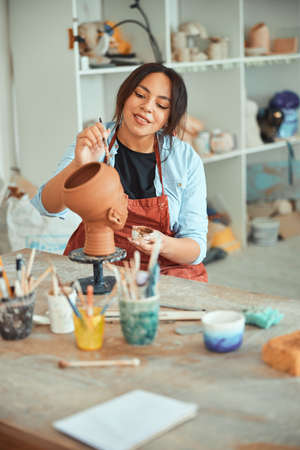 Charming female ceramist painting pottery in workshopの写真素材
