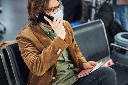 Stylish man in medical mask talking on cellphone at airportの写真素材