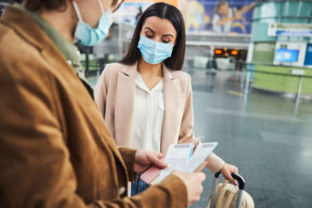 Young woman and man in medical masks checking tickets in airport
